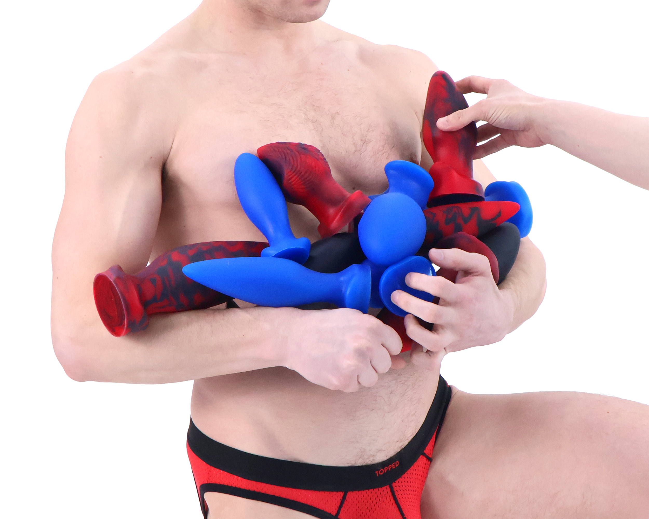 Topped Toys butt plugs in forge red, blue steel, and obsidian held by a model wearing a red and black jock strap against a white background.